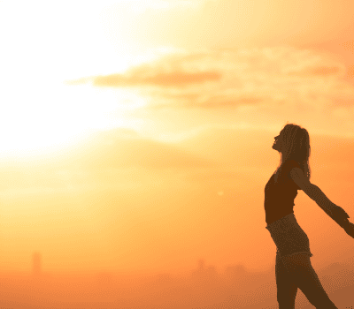 Frau steht im Sonnenuntergang und atmet Energie